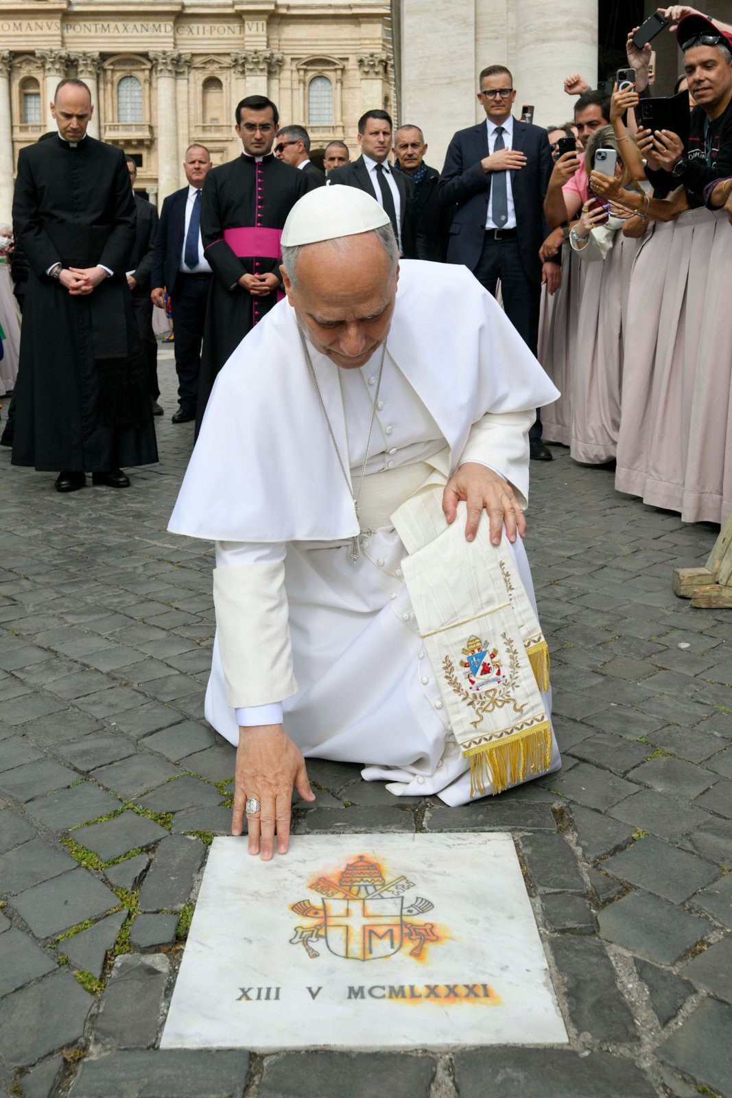 Pave Leo XIV berører plaketten som markerer stedet på Petersplassen der den hellige Johannes Paul II ble skutt i et attentatforsøk 13. mai 1981.